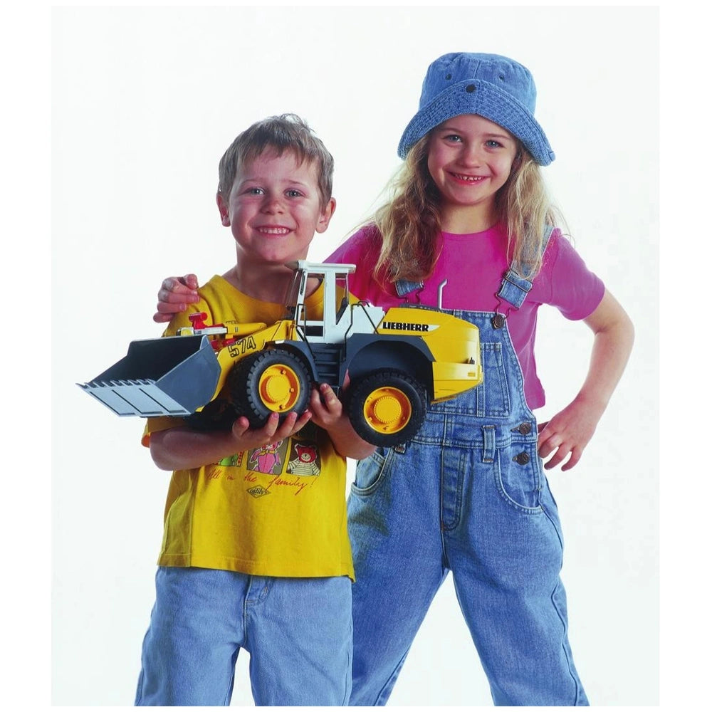Children smiling and holding a yellow Liebherr L574 toy loader with realistic details and front shovel.
