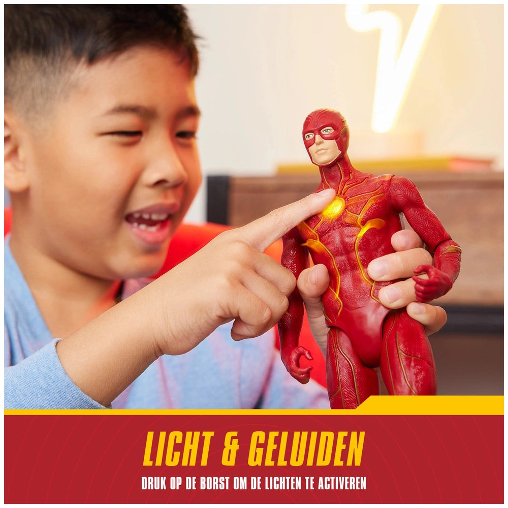 A young boy in a blue top points at a red Flash action figure with lights and sounds, showcasing excitement in a cozy indoor 