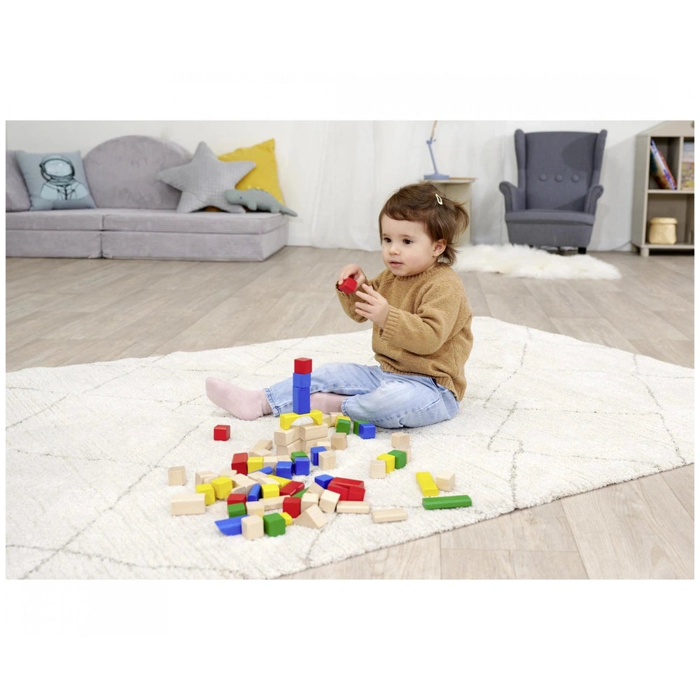 Eichhorn baby wooden colored blocks are scattered around a toddler sitting on a white rug in a cozy playroom setting.