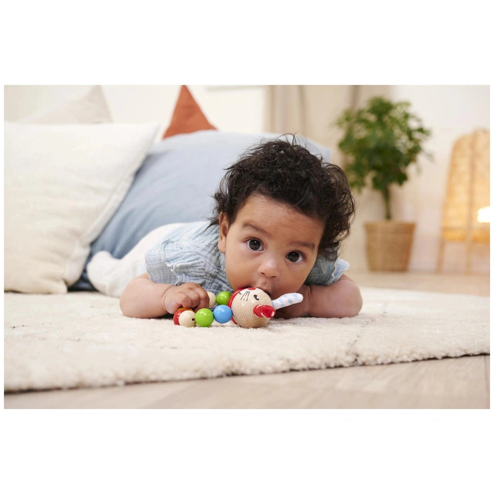 Eichhorn baby wooden teething ring rabbit beside a young child lying on a soft surface, looking at the camera.