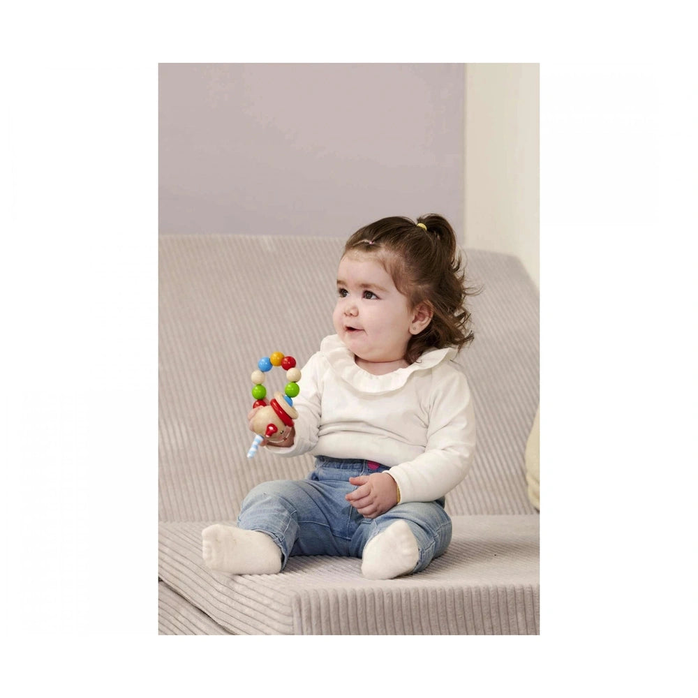 Eichhorn baby wooden teething ring rabbit held by a young child sitting on a light gray cushioned surface.