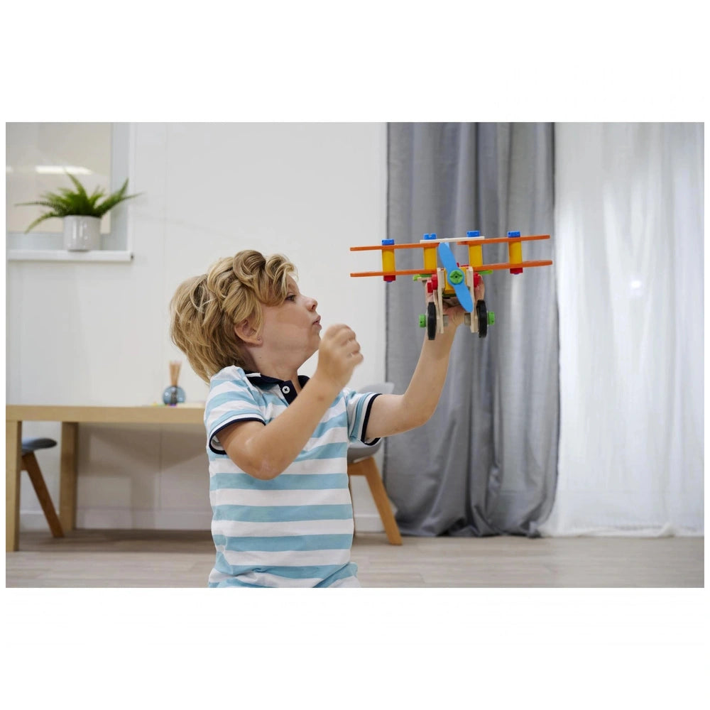 Eichhorn Constructor 4 in 1 construction set is featured as a young boy joyfully holds a blue and orange toy airplane indoors