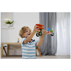 Child playing with a colorful toy vehicle in a bright room with wooden floors and a window in the background.