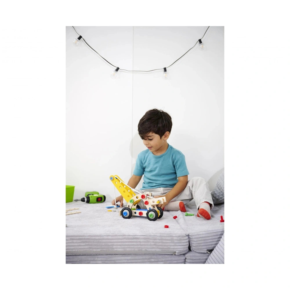 A young child in a blue shirt and white pants is engaged in play with the Eichhorn Constructor 4in1 construction set on a bed