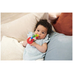 Eichhorn Eh Baby Wooden Teething Ring in use by a young child with dark hair lying on a couch, surrounded by soft cushions.