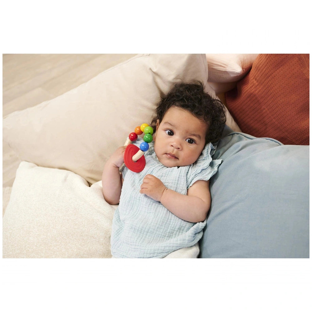 Eichhorn Eh Baby Wooden Teething Ring held by a baby in blue outfit, against a cozy indoor backdrop with soft colors.