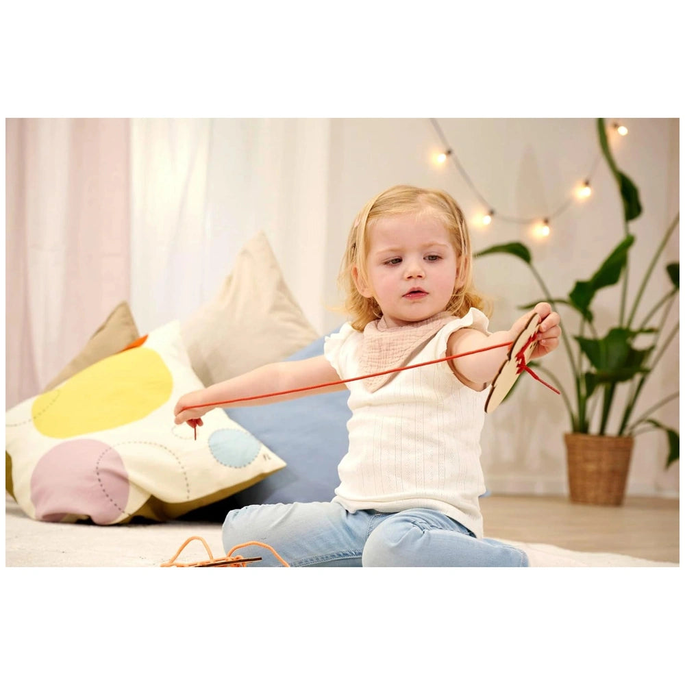 Eichhorn String Game - A young girl plays with a red string toy in a cozy, colorful indoor space.