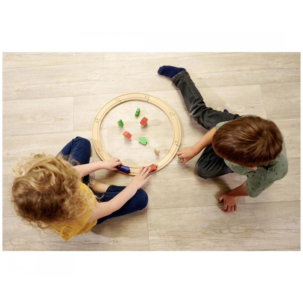 Eichhorn Train Track Playset featuring two children playing with colorful wooden trains on a light wooden floor.