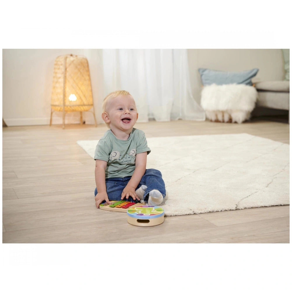 Eichhorn wooden drum and xylophone set with a smiling child playing on a light rug in a cozy, neutral-colored room.