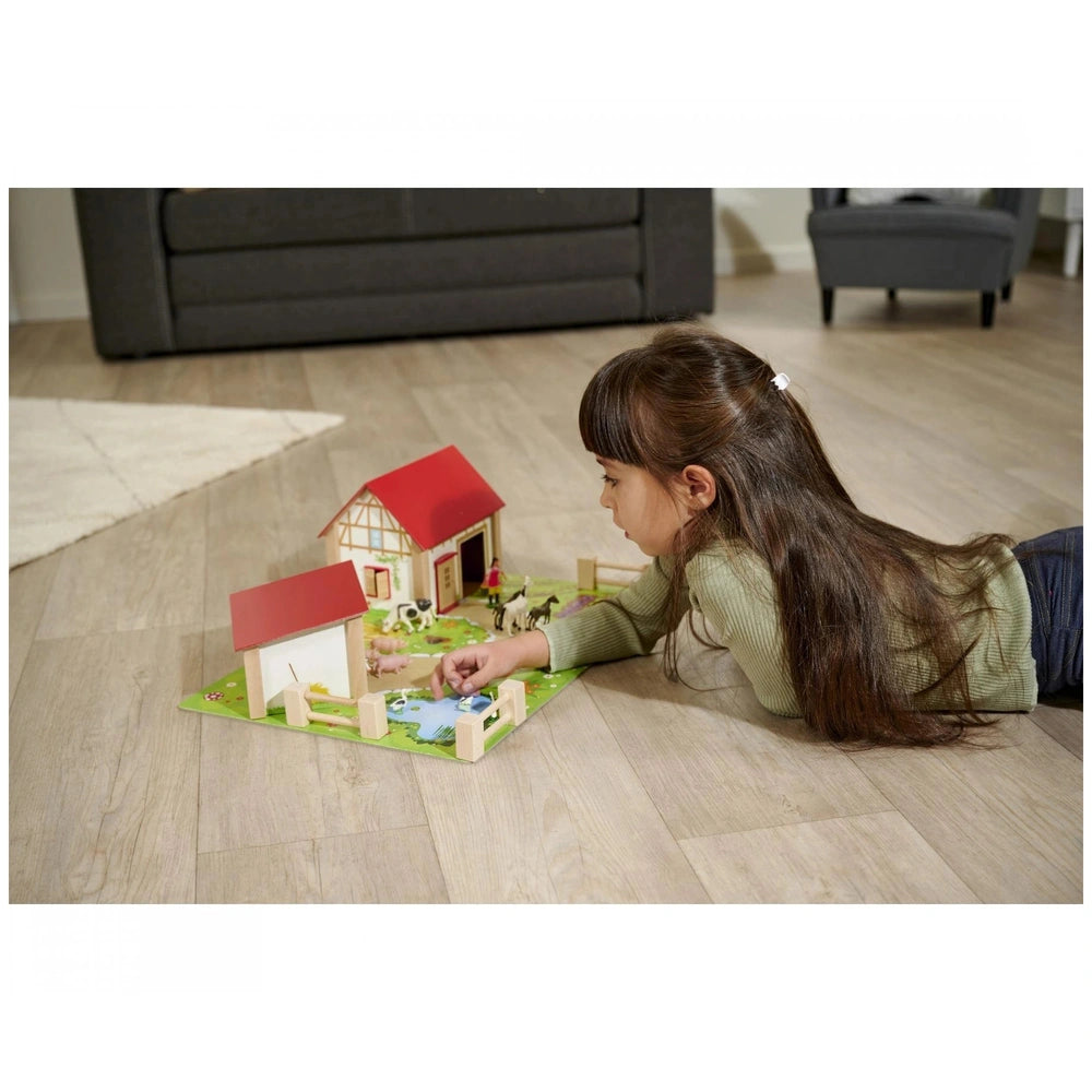 Eichhorn Wooden Farm set displayed with a girl playing on the floor, featuring a barn, house, animals, and accessories.