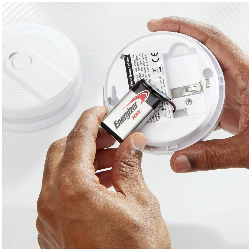 Energizer Max 6LR61 9V battery in black and red casing, placed in a white smoke detector with a clear plastic window.