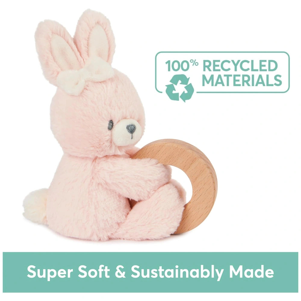 Pink bunny soft toy holding a light brown wooden ring, featuring floppy ears and a bow, set against a plain white background.