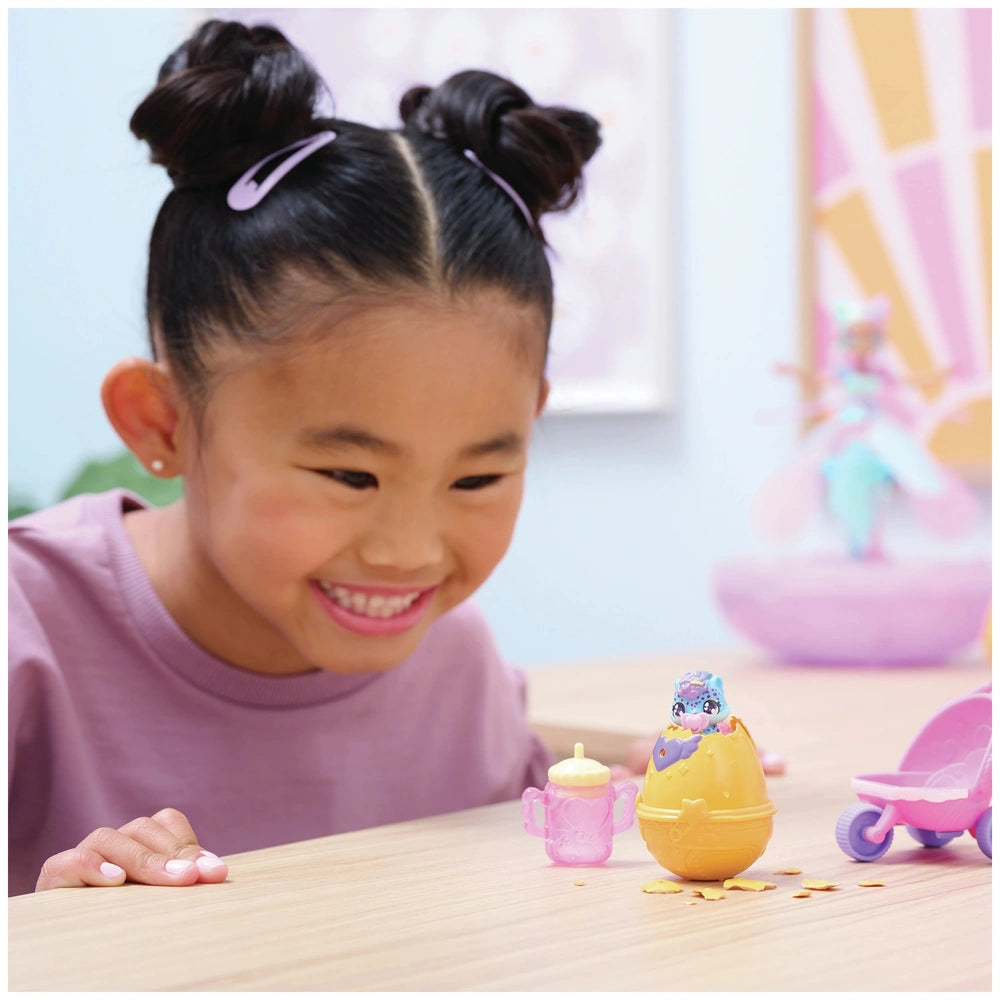 Hatchimals Alive Hatch N’ Stroll Playset displayed on a table with a smiling girl engaging in play with colorful toys.