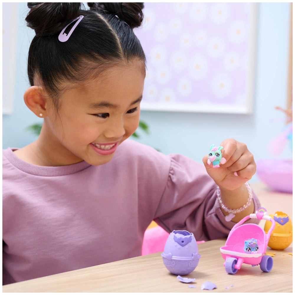Hatchimals Alive Hatch N’ Stroll Playset with stroller and two mini figures, enjoyed by a smiling girl at a table.