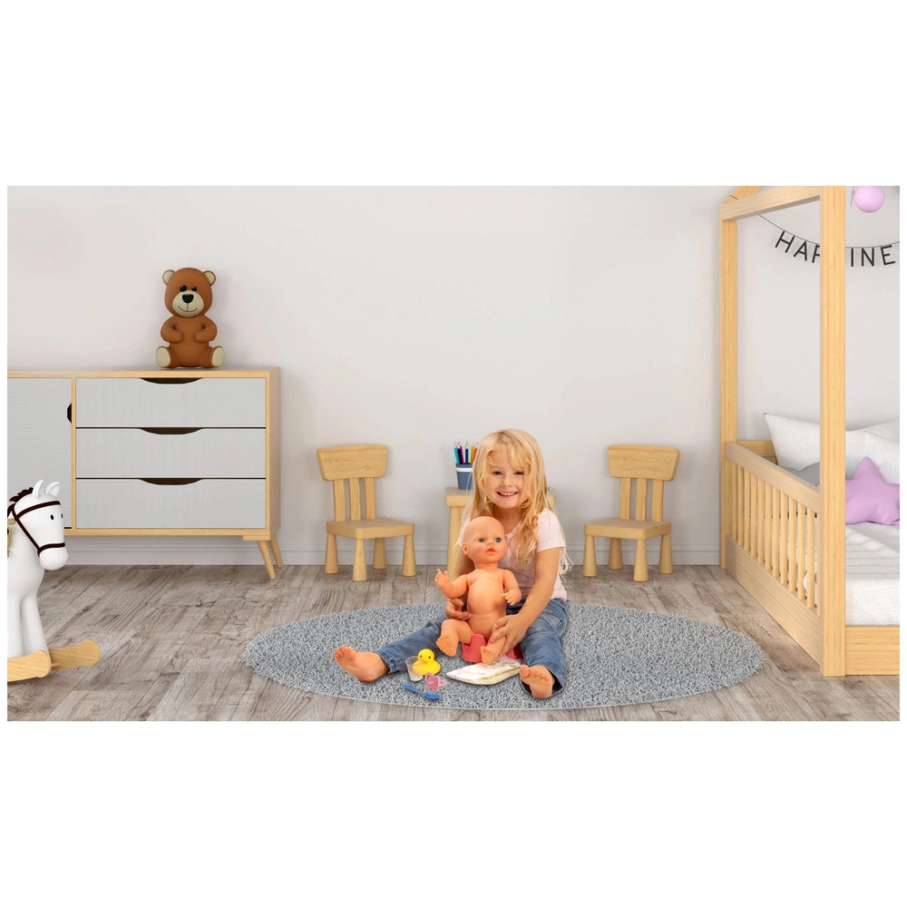 Heless potty with accessories beside a young girl holding a doll, surrounded by wooden furniture and a gray carpet.