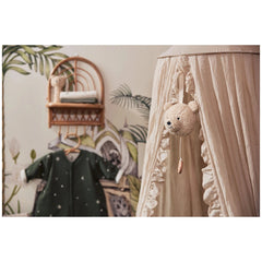 Jollein musical hanger featuring a teddy bear suspended from a white curtain against a green fabric backdrop on a wooden shel