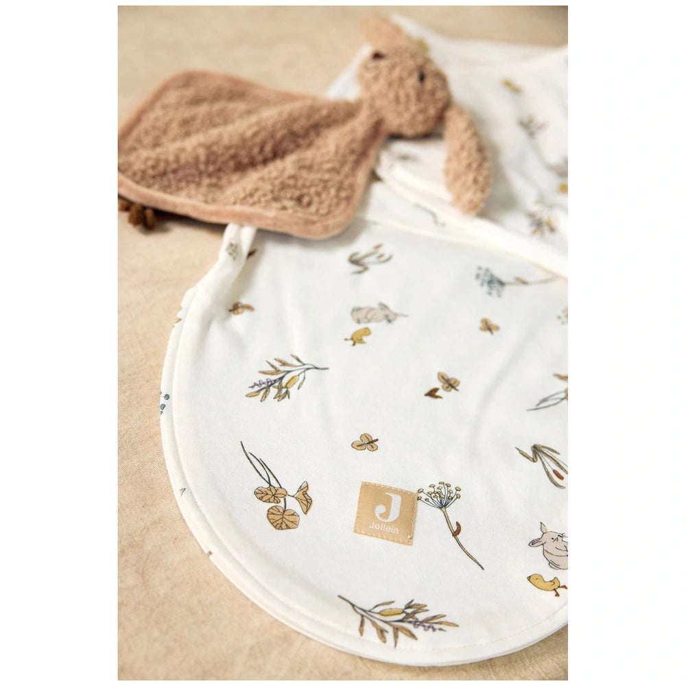 Jollein pacifier cloth bunny in light brown placed on a white patterned blanket with a soft textured fabric.