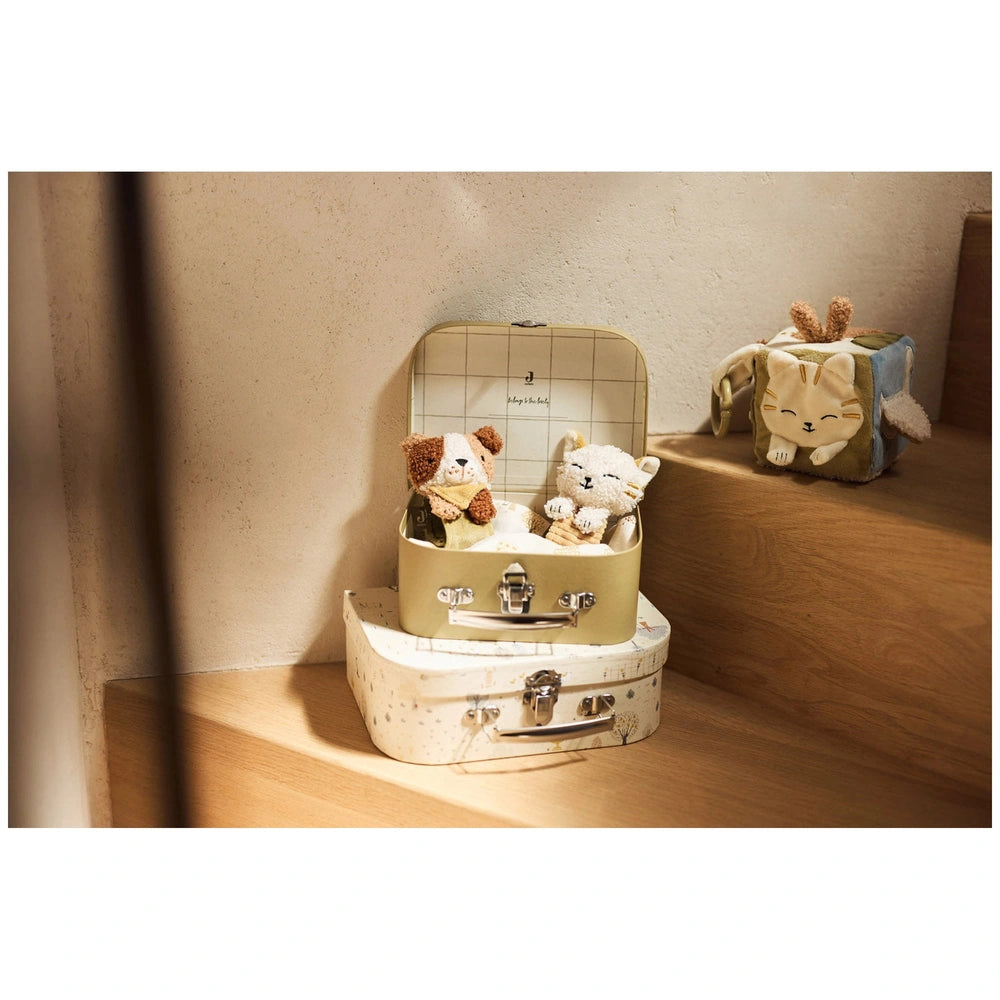 Jollein Wrist Rattle Tiny Park Charlie Cat Rattles displayed on a light suitcase with two soft teddy bears on a wooden floor.