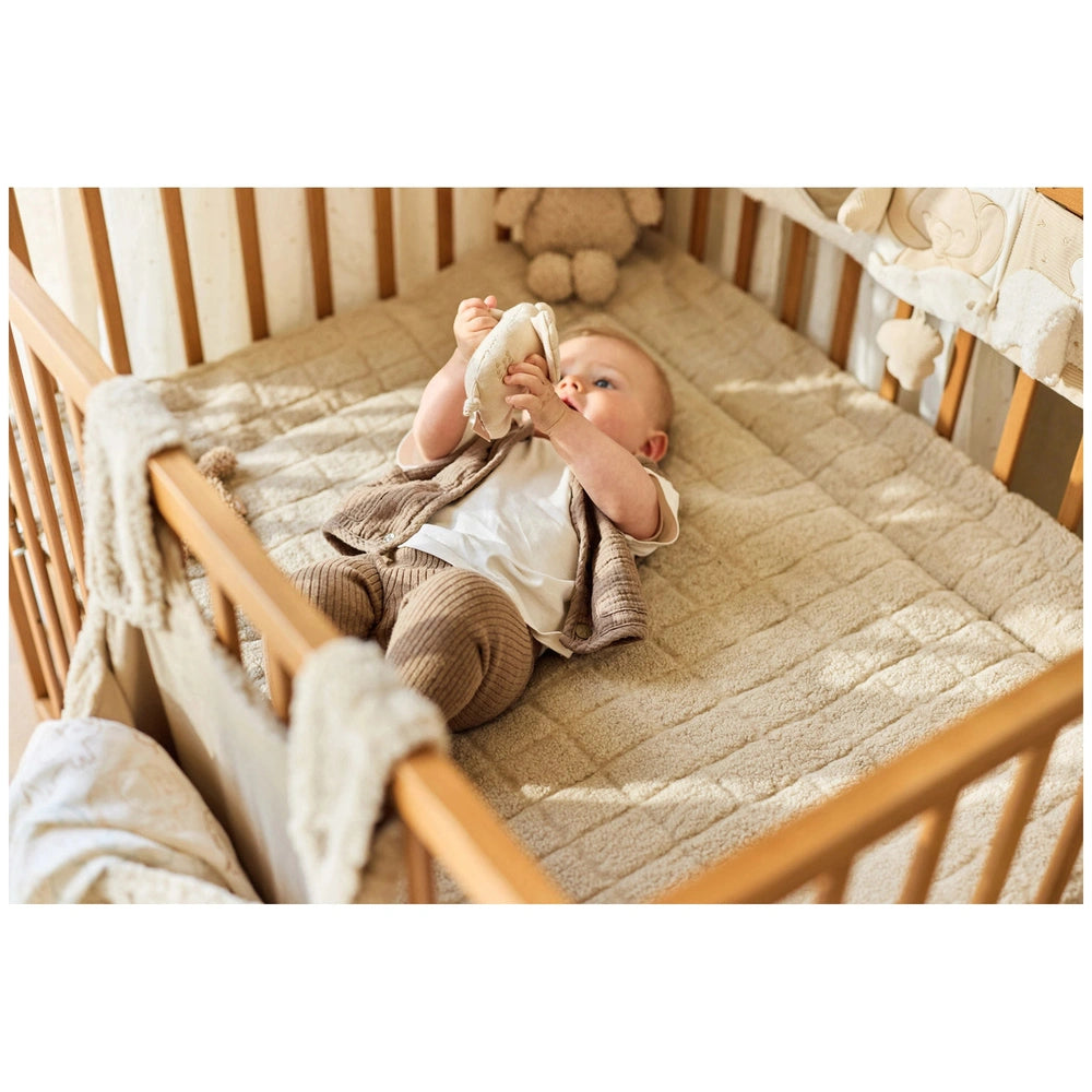 Jollein Wrist Rattle Tiny Park Charlie Cat rests in a baby’s crib with light beige fabric, featuring a white mattress and can