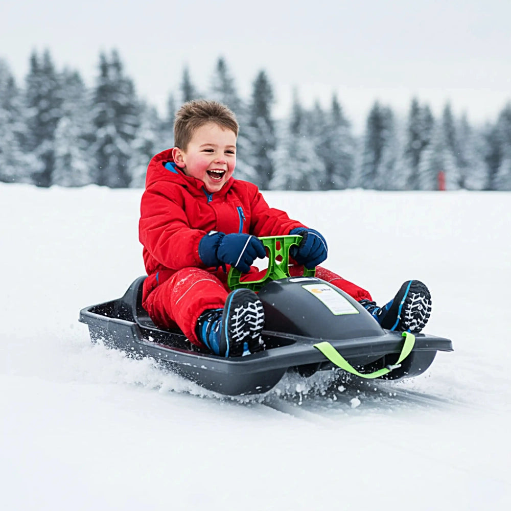 Child in red snowsuit on black KHW Snow Fox sled with green attachment in a snow-covered landscape.