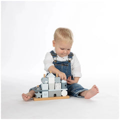Child in blue overalls and white shirt plays with colorful wooden stacking blocks on a white surface.