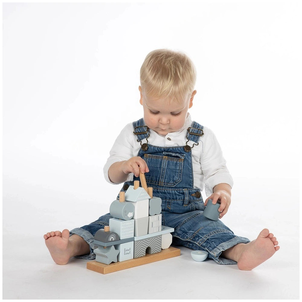 Label-Label stacking blocks house with a child in a denim jumpsuit, holding gray interlocking pieces on a white surface.