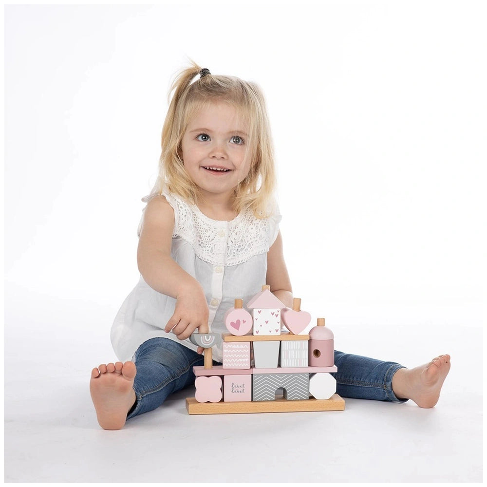 Label-Label stacking blocks house toy, blonde girl in white top and blue jeans, smiling while holding a wooden block with sha