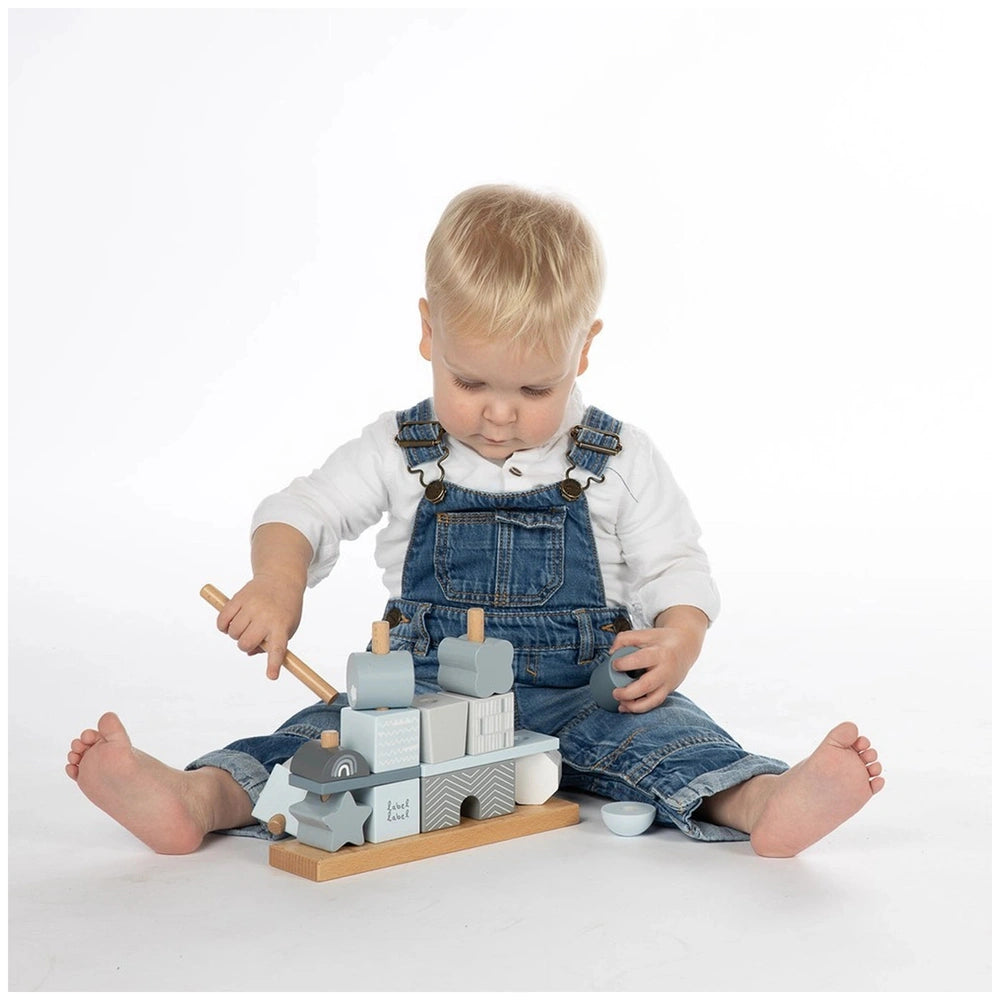 Label-Label stacking blocks house with a young child in blue denim overalls playing on a wooden toy train track.