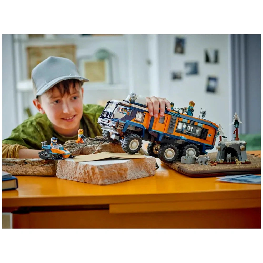 LEGO Arctic Explorer Science Lab Truck in orange and blue is held by a smiling boy at a wooden table with a cardboard box.