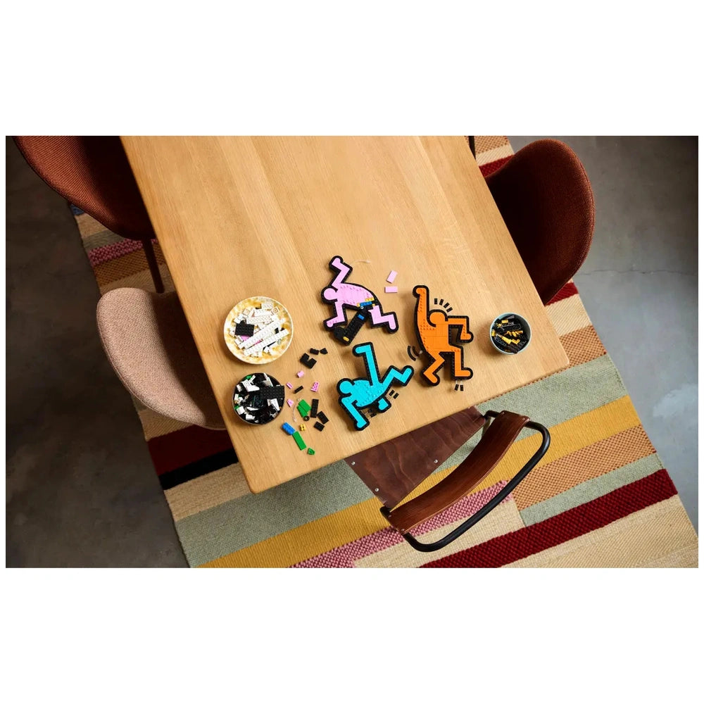 LEGO Art Keith Haring Dancing Figures set displayed on a wooden dining table with colorful items scattered around.