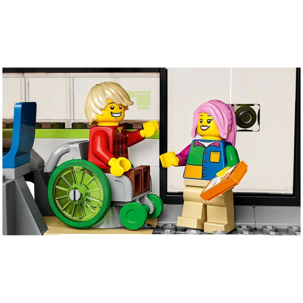 Two LEGO minifigures interact inside a train car, one in a green wheelchair and the other holding an orange box. The setting features a modern, light-colored interior with seating and a food prep area.