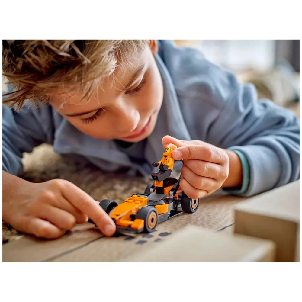 Young boy focused on assembling a LEGO® McLaren race car, holding the driver minifigure with a bright orange and black design.