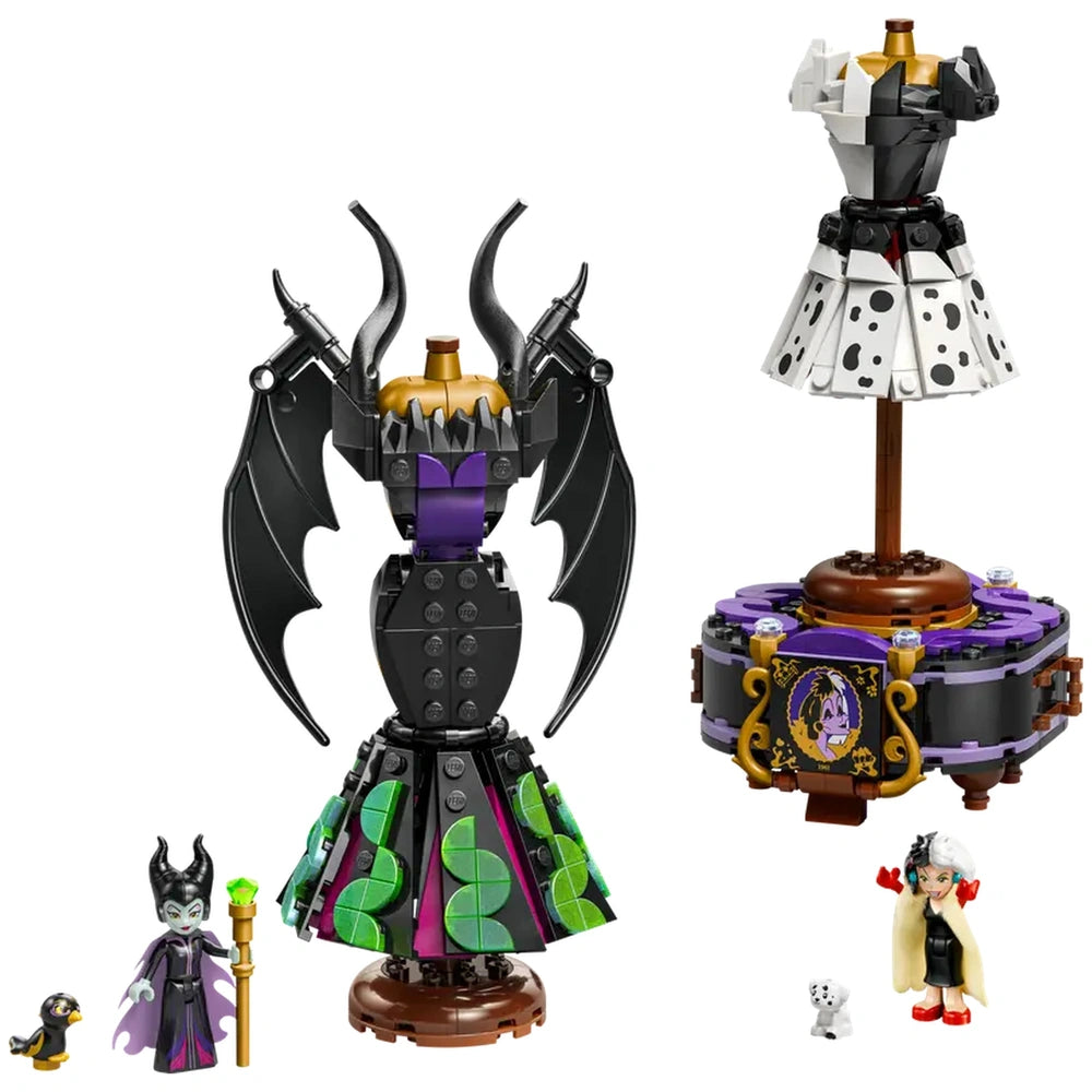 Two detailed dress models representing Maleficent and Cruella De Vil. Maleficent's dress features black wings and a green and purple skirt, while Cruella's dress is black and white with a polka dot pattern. Both dresses are displayed on elegant stands, accompanied by minifigures of the characters and their pets.