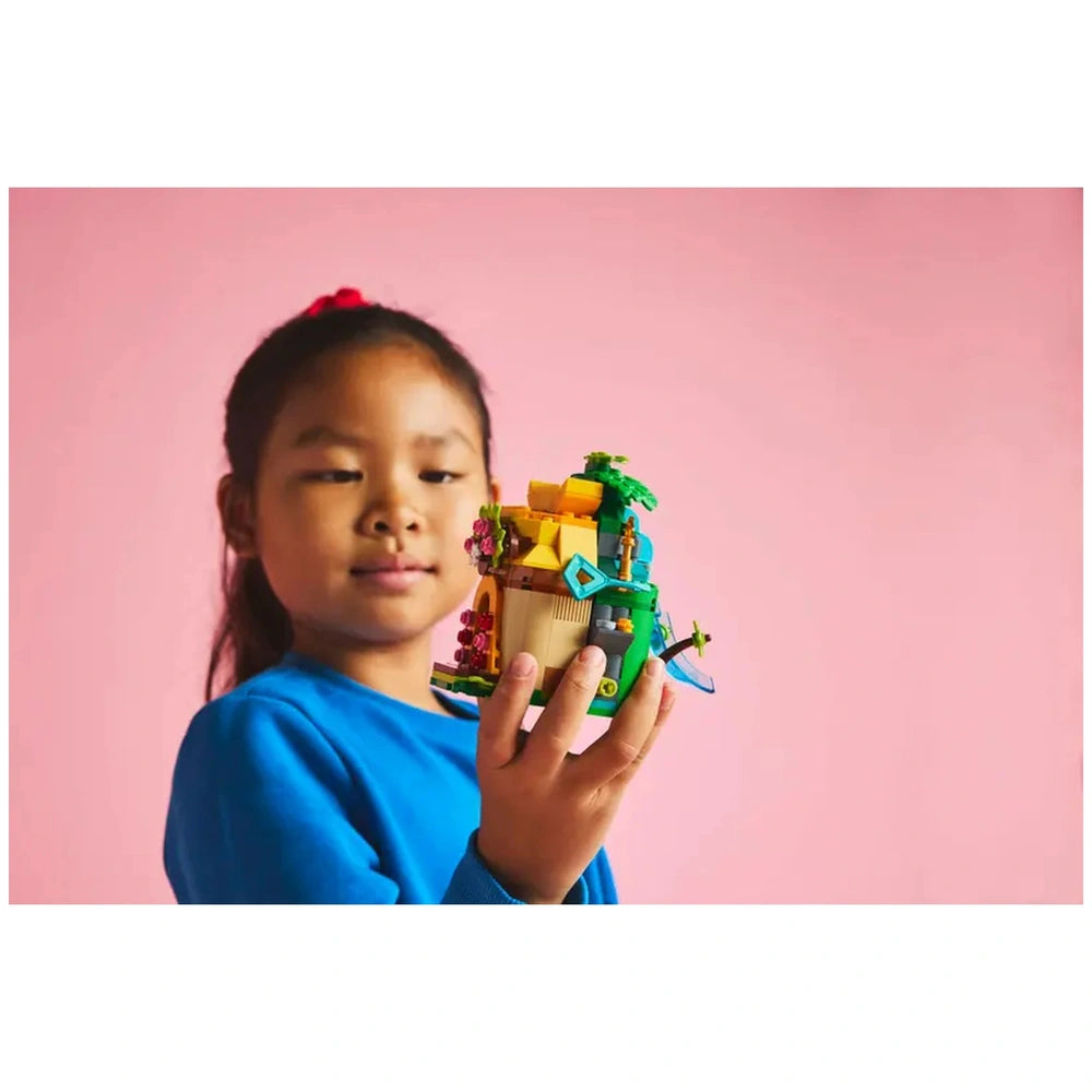 A child holding LEGO® Disney Moana’s Island Fun construction set, featuring colorful designs, palm trees, and flowers, against a pink background.