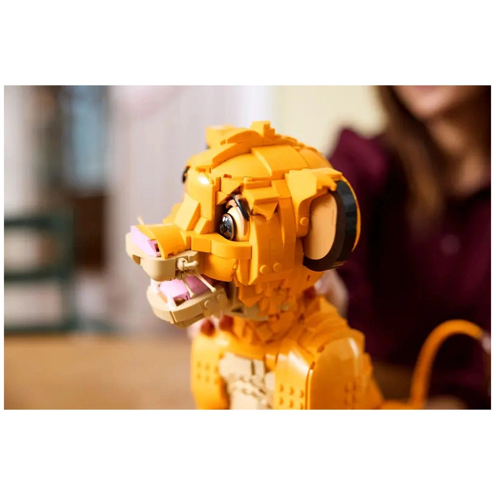Young Simba Lego construction set, featuring vibrant orange colors, movable head, and detailed facial features, displayed on a table.
