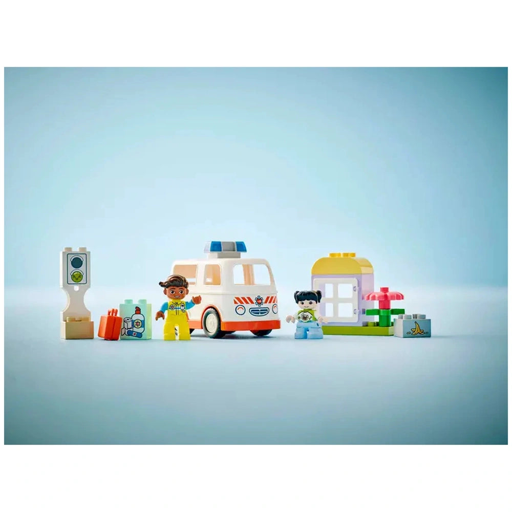 LEGO® DUPLO® Ambulance & Driver set featuring a smiling paramedic in yellow and a girl in blue, alongside an ambulance toy, traffic light, and fun building elements against a soft blue background.