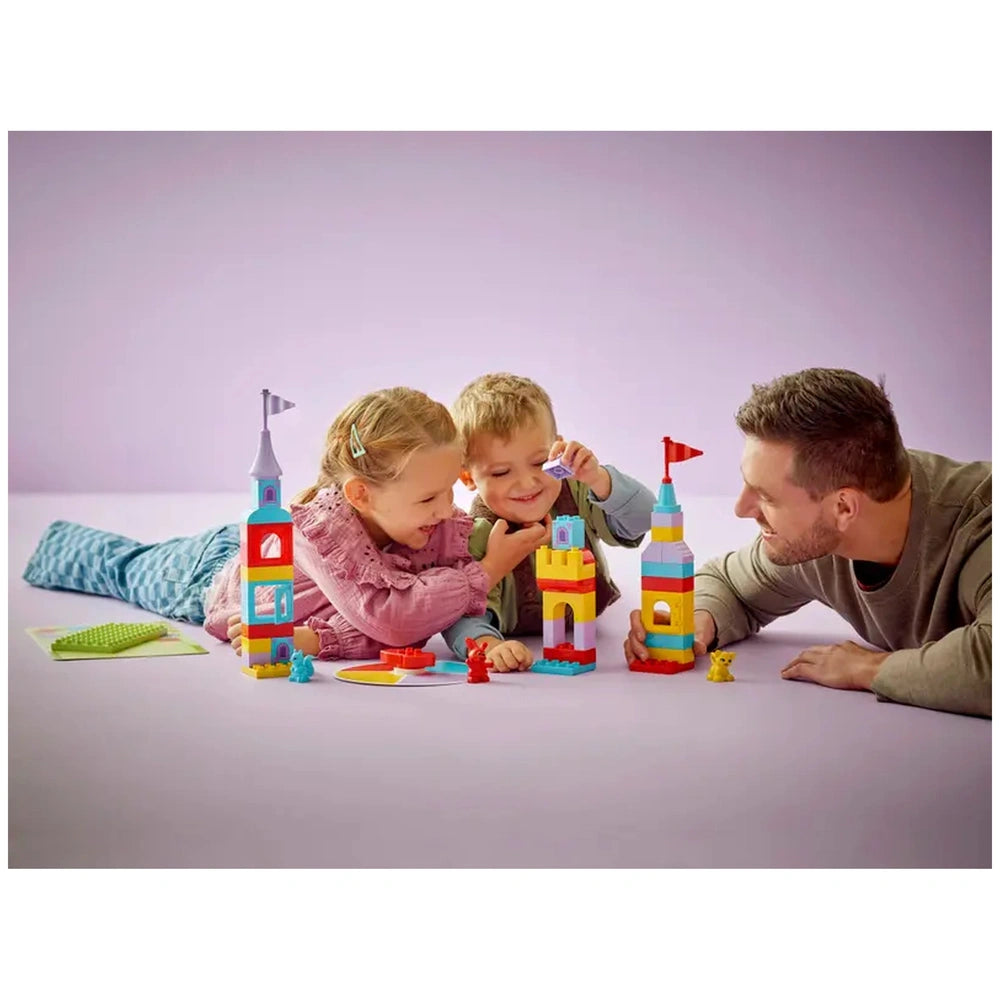 Two children and an adult engage with the colorful LEGO® DUPLO® Hopsy’s Castle Game on a light purple background, building vibrant castles and smiling collaboratively.