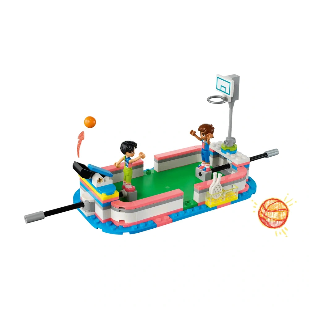 Two LEGO mini-dolls celebrate in a colorful sports center, featuring a green field, a basketball hoop, and assorted sports equipment.