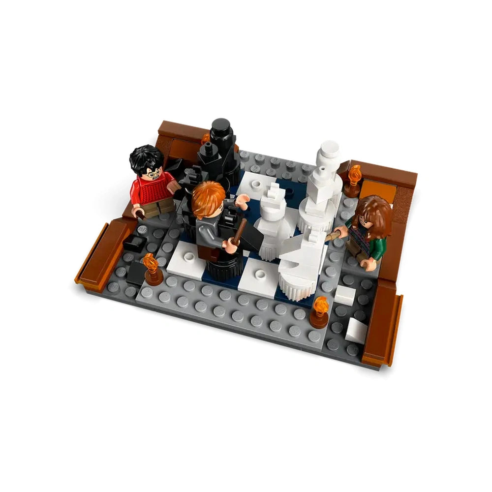 Four LEGO figures, resembling Harry, Ron, Hermione, and a black knight, are engaged in a wizard chess game on a gray and white checkerboard base with decorative torches.