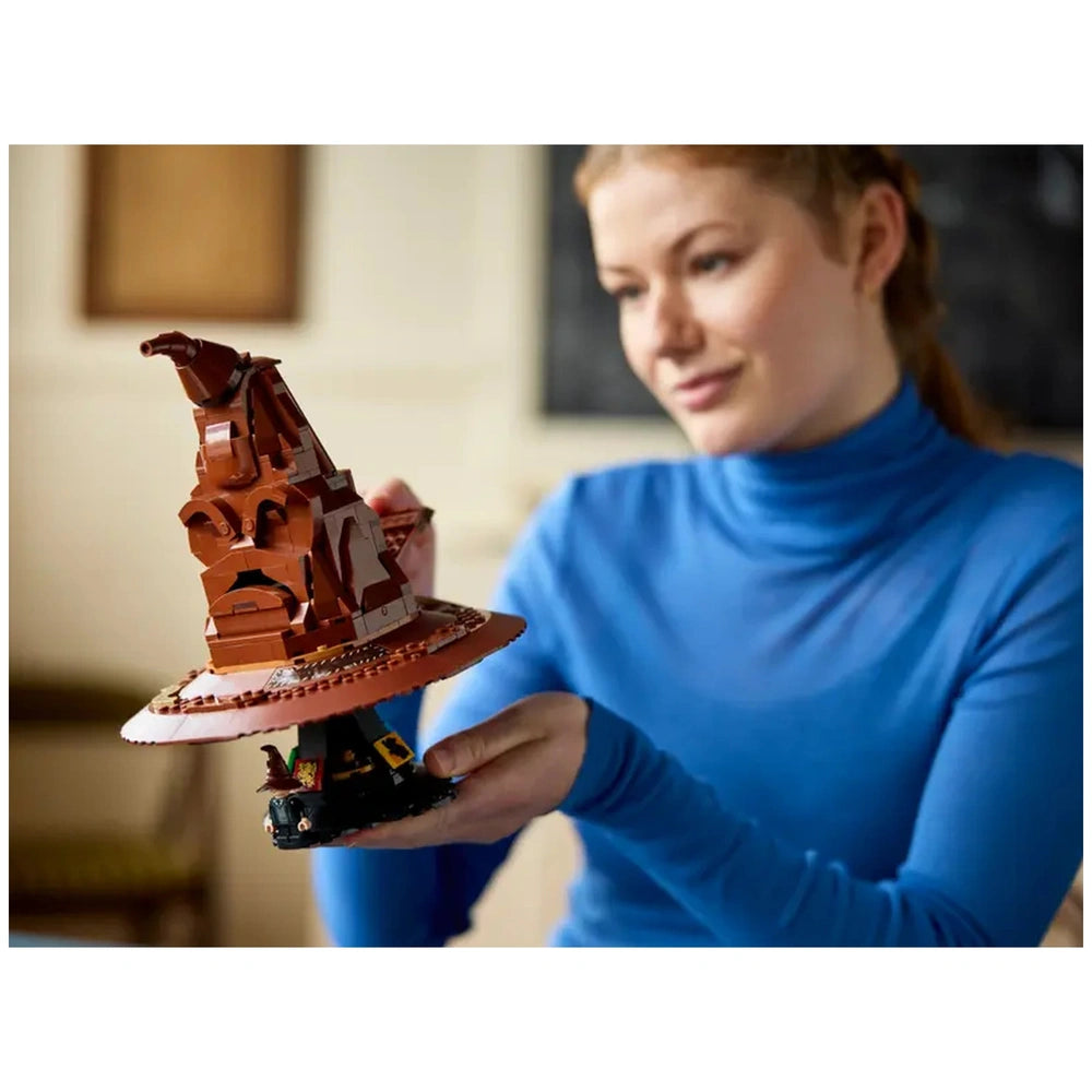 A woman in a blue turtleneck holds a detailed LEGO Talking Sorting Hat, showcasing its intricate design and vibrant colors against a soft, blurred background.