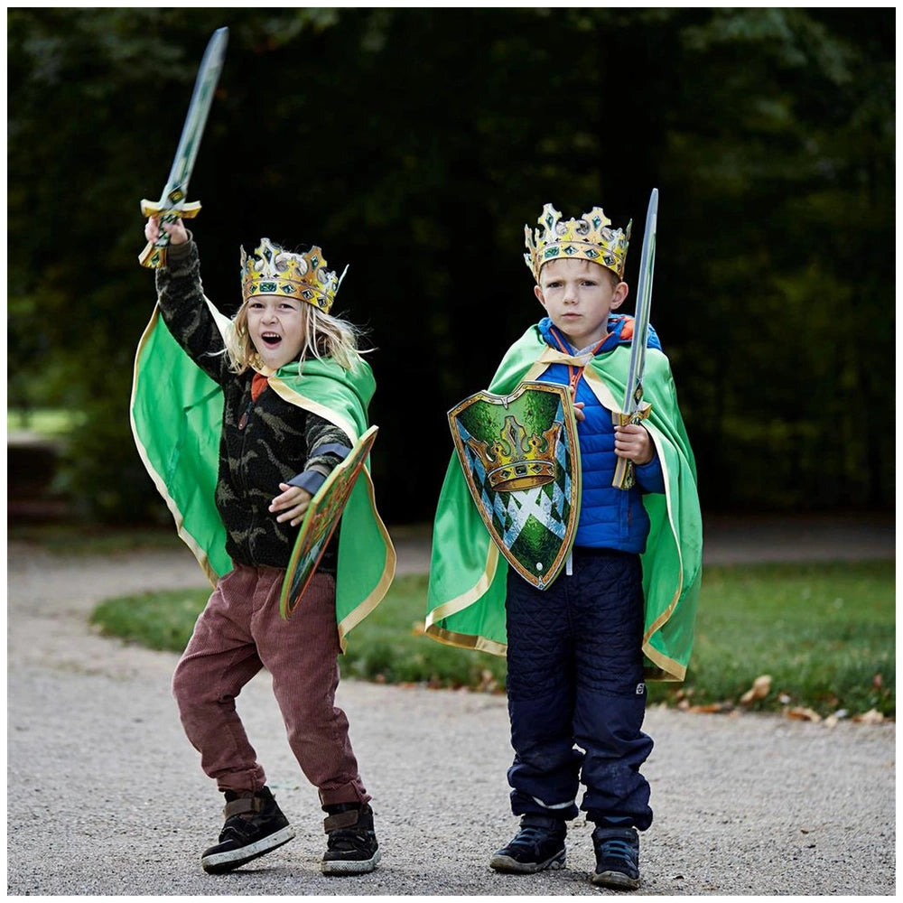 Two children in shiny green and gold Liontouch capes wielding metallic toy swords in a playful role-playing scene.