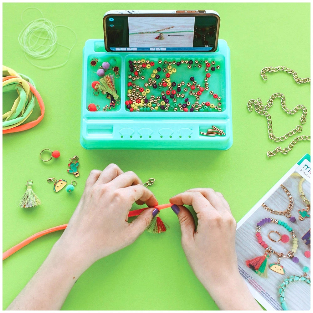 MAKE IT REAL Neo-Brite Chains and Charms kit featuring colorful beads on a blue tray atop a green surface.