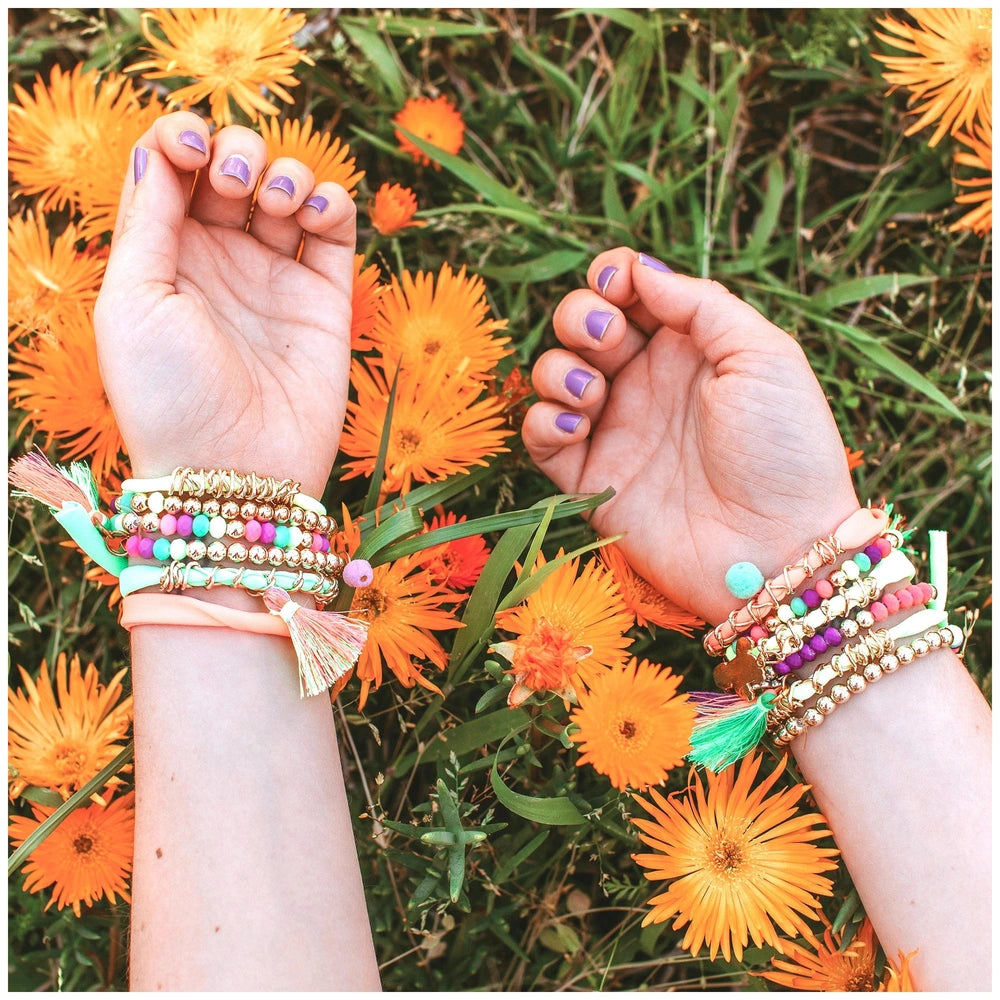 Neo-Brite Chains and Charms in a close-up lifestyle scene with hands, orange flowers, green leaves, and purple nail polish.