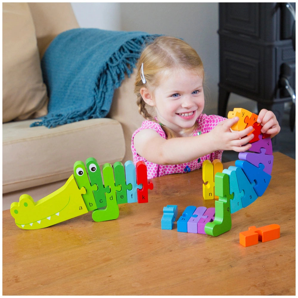 Crocodile Alphabet Puzzle on a wooden table with a young girl wearing a pink top and white headband in a cozy living room.