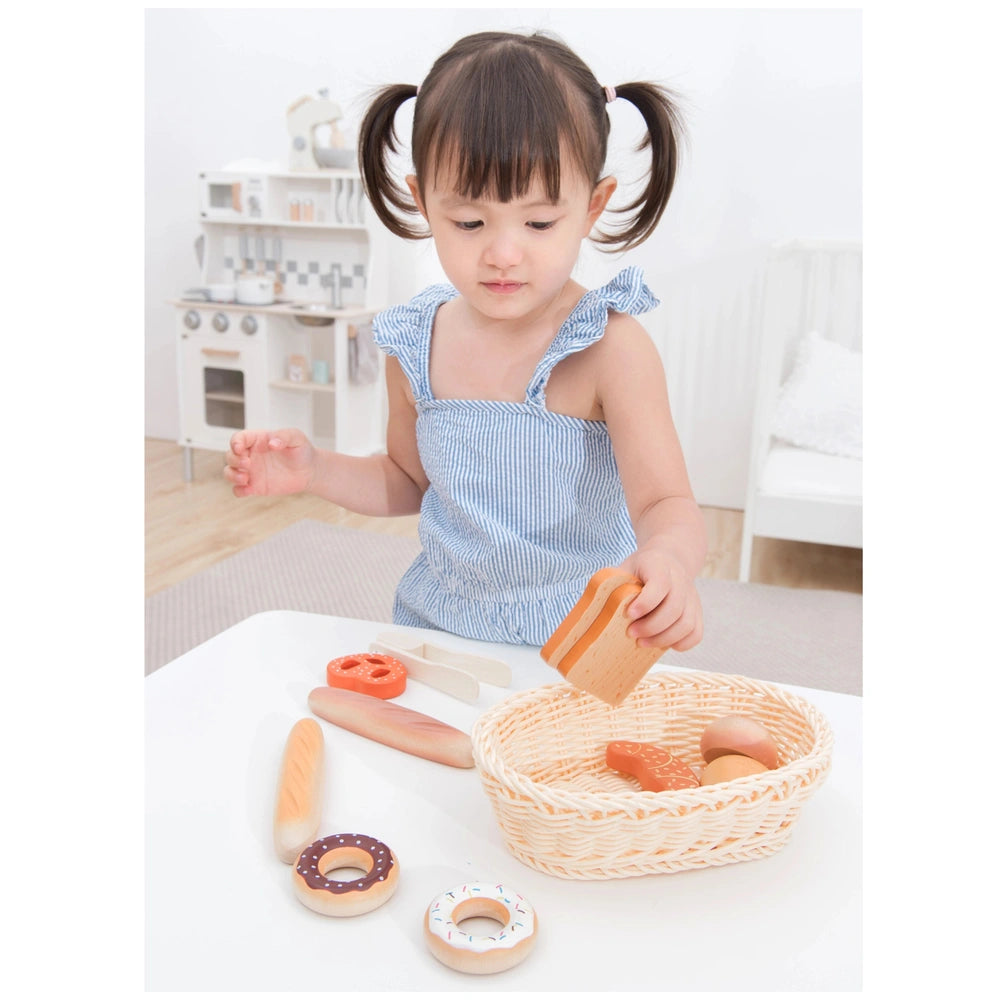 New Classic Toys bread basket set featuring plastic utensils, doughnut toy, and eggs on a wooden table in a lifestyle scene.