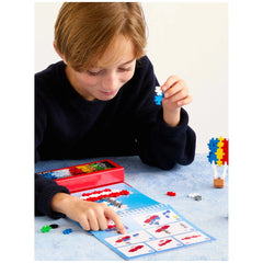 Plus Plus transportation activity pad with a child’s hand holding a glossy blue and red toy on a blue matte table.