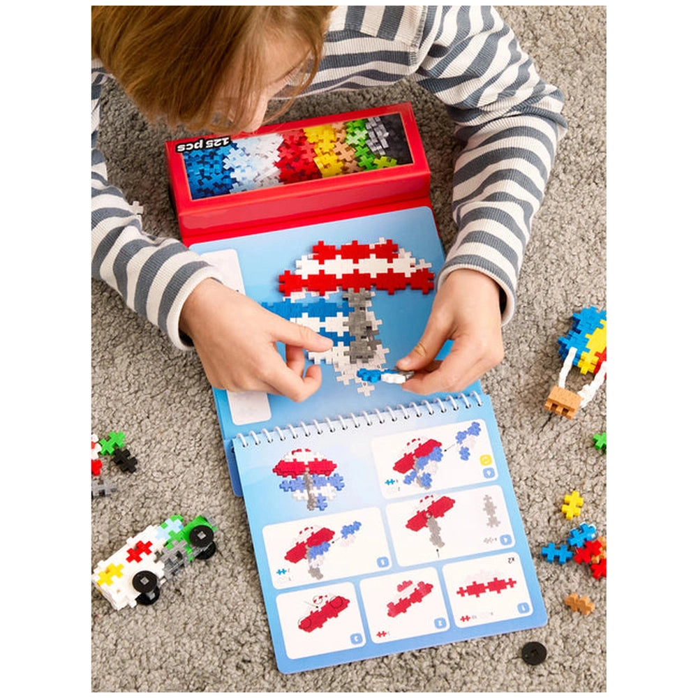 Plus Plus transportation activity pad features a child playing with red Lego pieces on a blue baseplate, surrounded by scatte