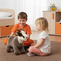 Rudy Little Mountain Chamois plush sits on a textured carpet with two children in colorful clothing smiling beside it.