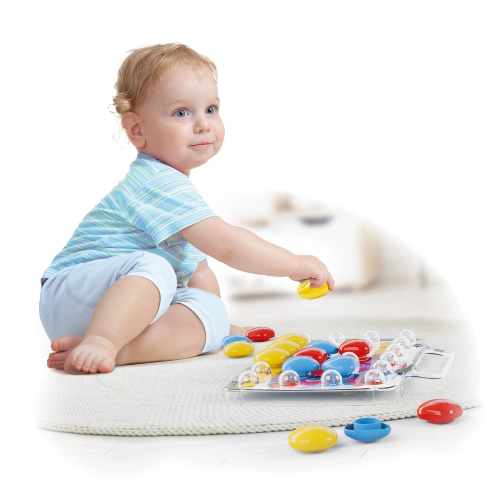 Quercetti FantaColor Baby activity toy with a child in a blue striped shirt holding a yellow object surrounded by colorful ba