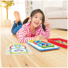 Quercetti FantaColor Tab toy with colorful components, a young girl coloring on a page, and a red tray on wood flooring.